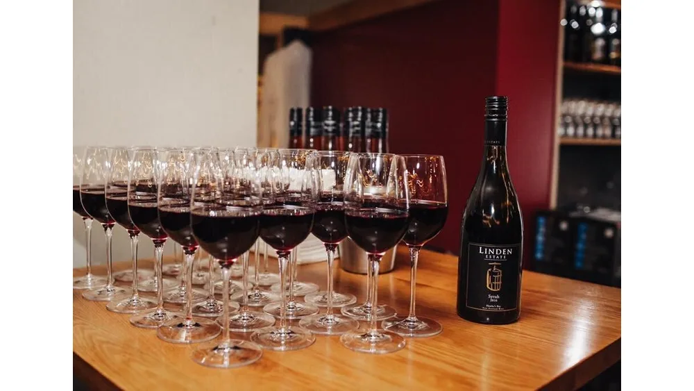 Hàng ly vang đỏ trên quầy gỗ bên chai Linden Estate Syrah 2016 chuẩn bị cho buổi thử rượu