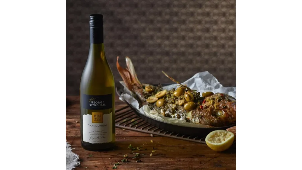 Chai vang trắng Chardonnay George Wyndham Bin 222 đặt cạnh đĩa cá nướng và nửa quả chanh